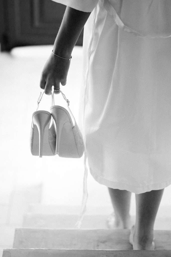 photo de mariée qui descend les escaliers et tient ses chaussures pendant les préparatifs de son mariage