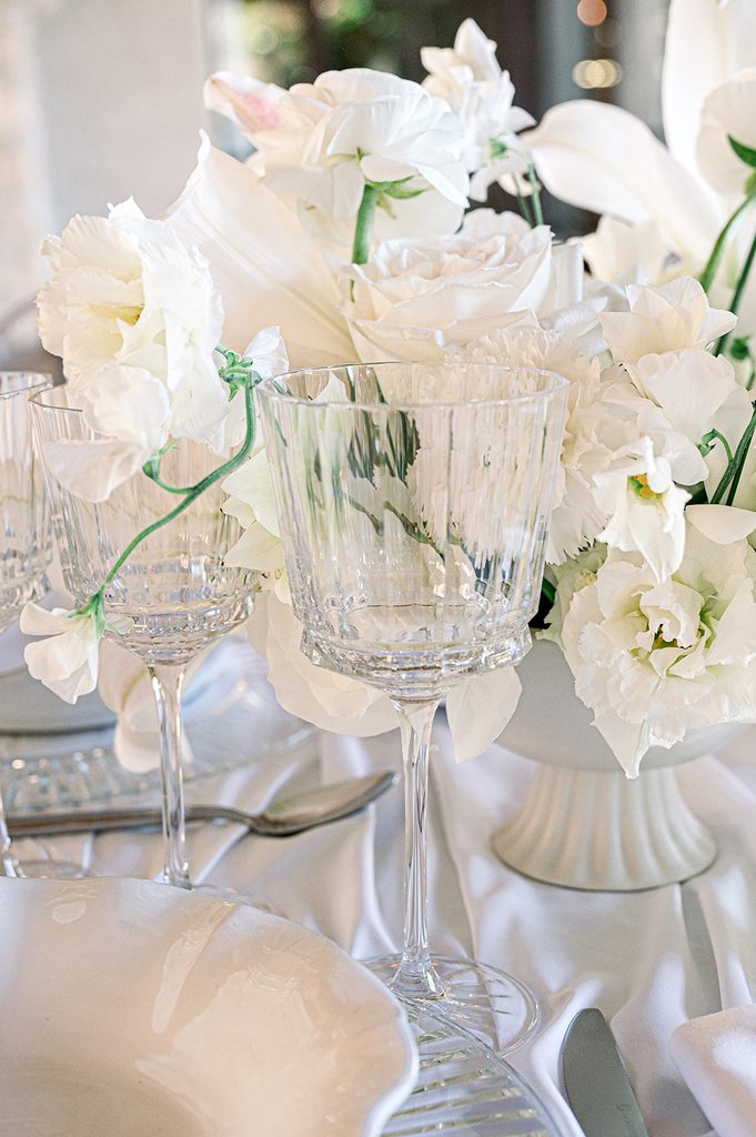 verre à pied en cristal devant une décoration florale blanche pour un mariage de luxe au Mas de la Rose en Provence 