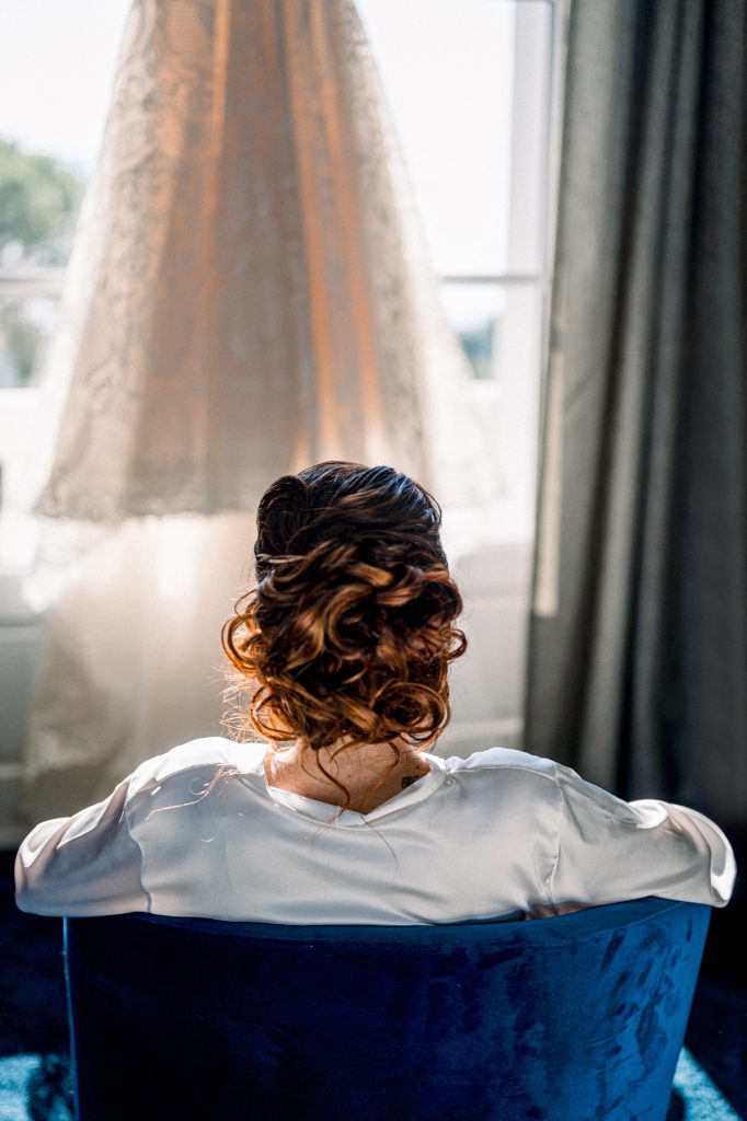 mariée de dos qui regarde sa robe accrochée à la fenêtre du Castel Bay
